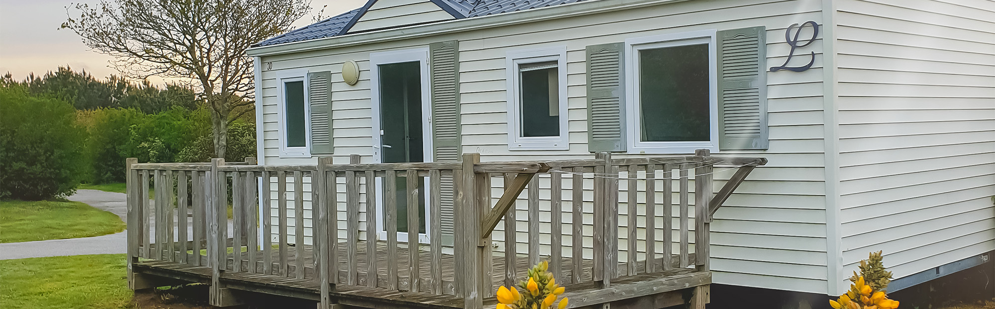 Mobil-home avec terrasse en bois, environnement verdoyant.